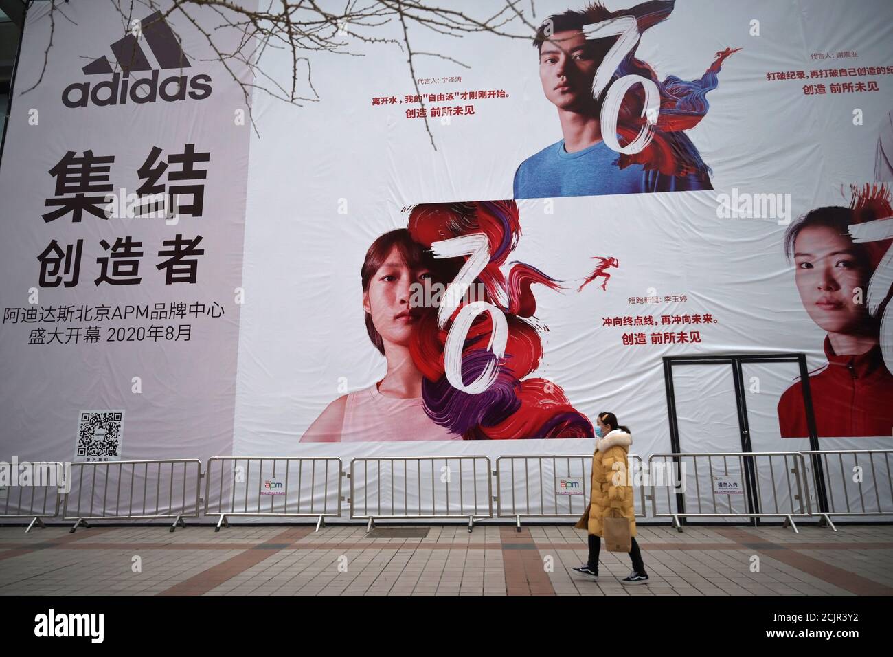 A woman wearing a face mask walks past a banner advertising new Adidas  store, as the country is hit by an outbreak of the novel coronavirus, in  Beijing, China February 20, 2020.