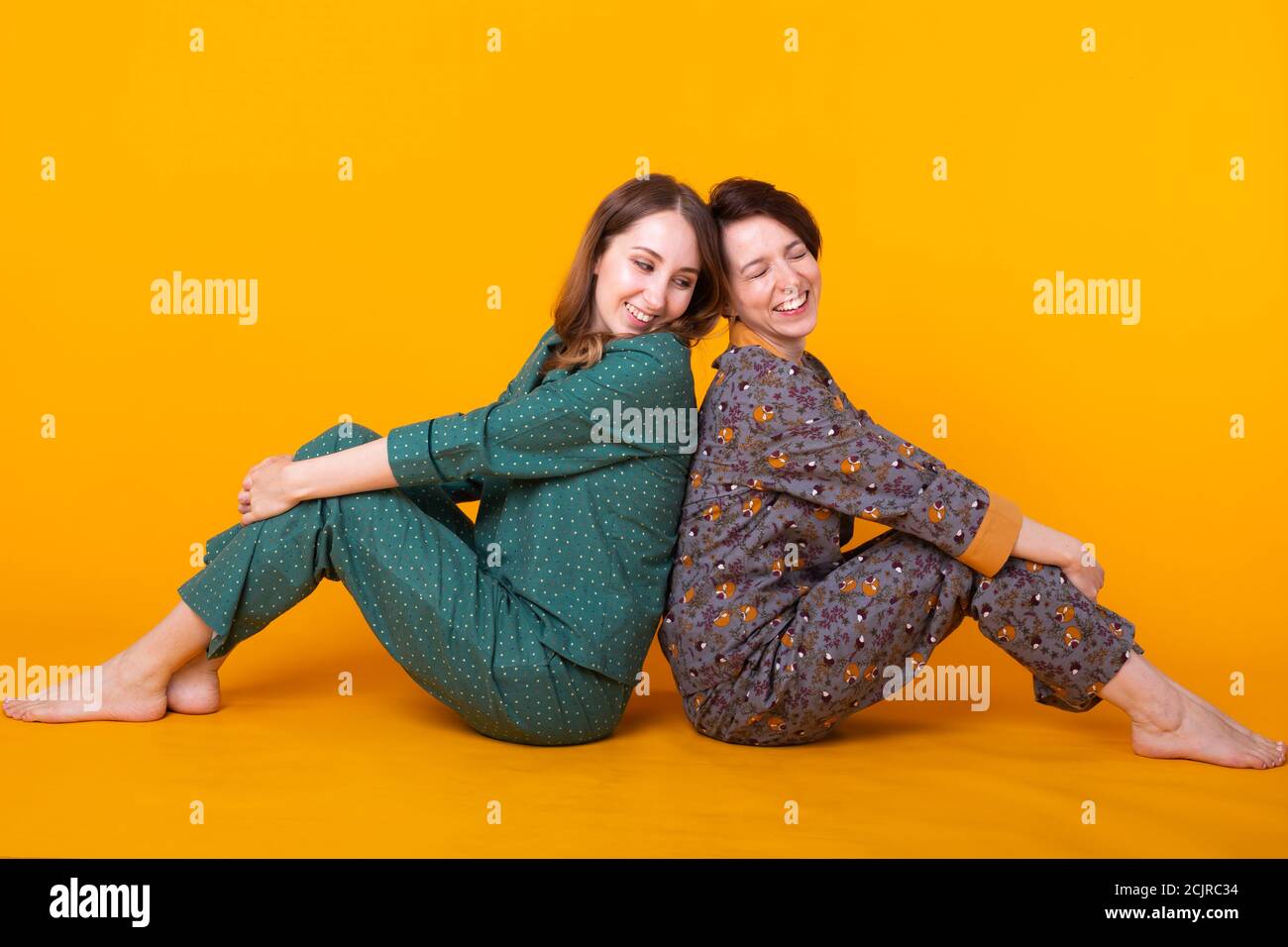 Portrait of two beautiful young girls wearing colorful pyjamas having fun during sleepover isolated over yellow background. Pajama party and hen party Stock Photo Alamy