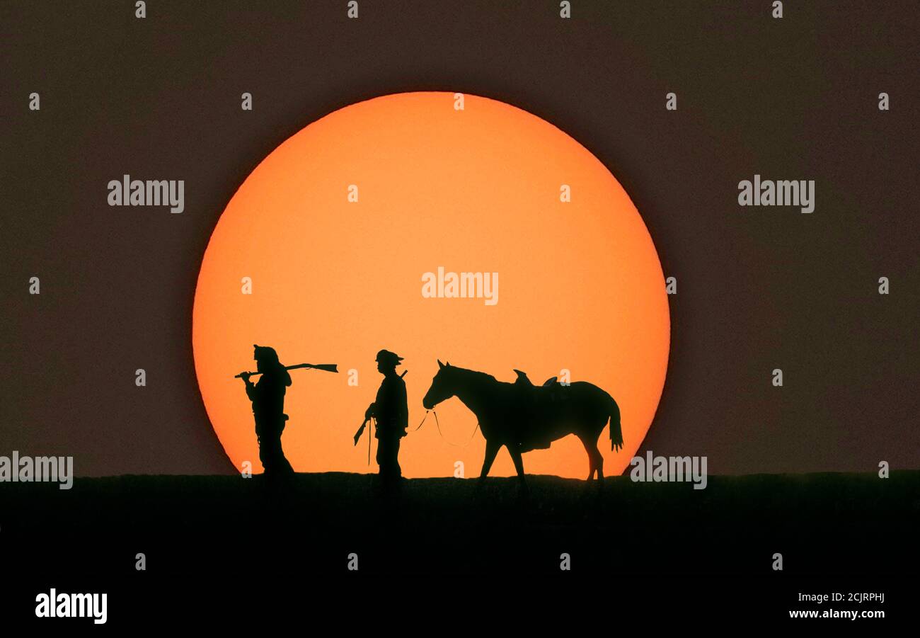 Mountain men leading a horse  silhouetted against a setting sun. Stock Photo