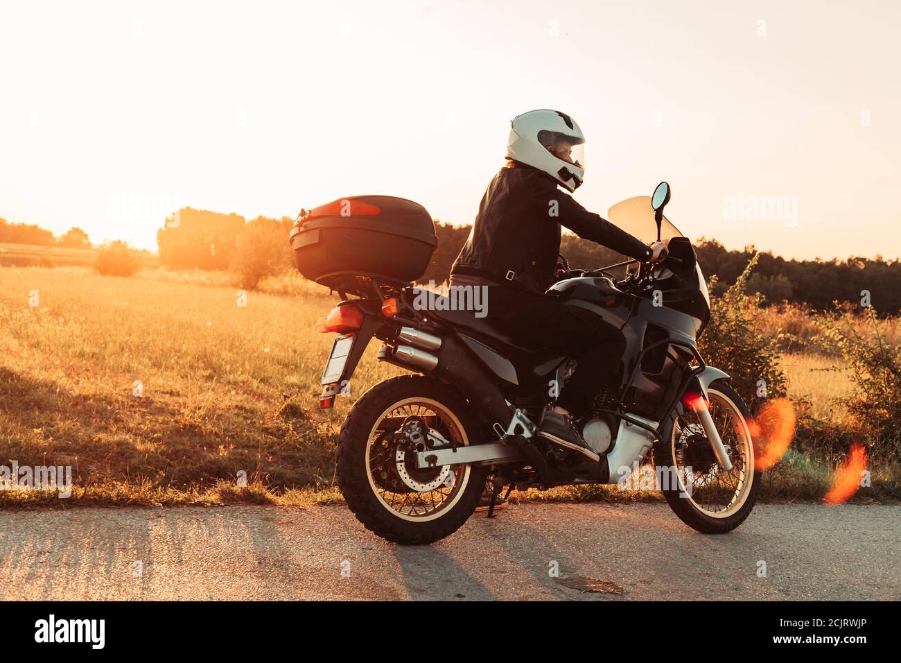 Female biker sits on the bike, takes a rest. Afternoon light, copy space Stock Photo