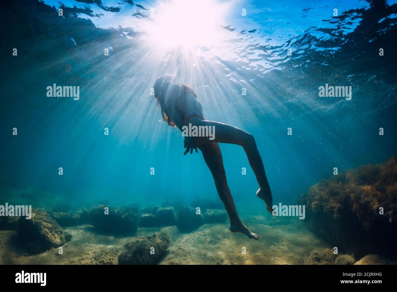 Attractive woman dive near stone with seaweed in underwater. Swimming ...