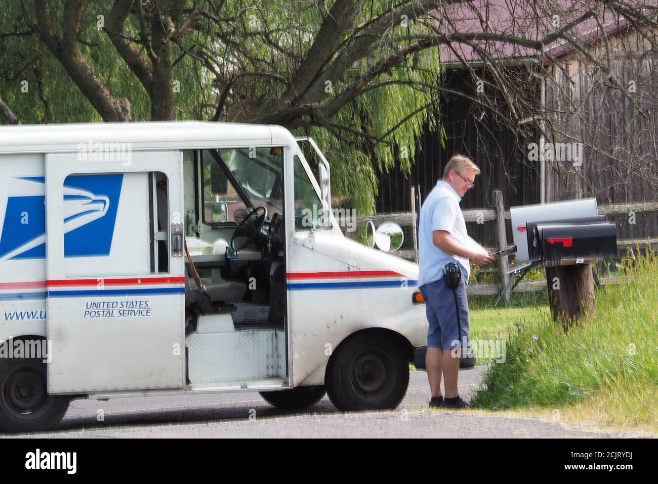 The postman is delivering the mail and is standing by the truck. Stock Photo