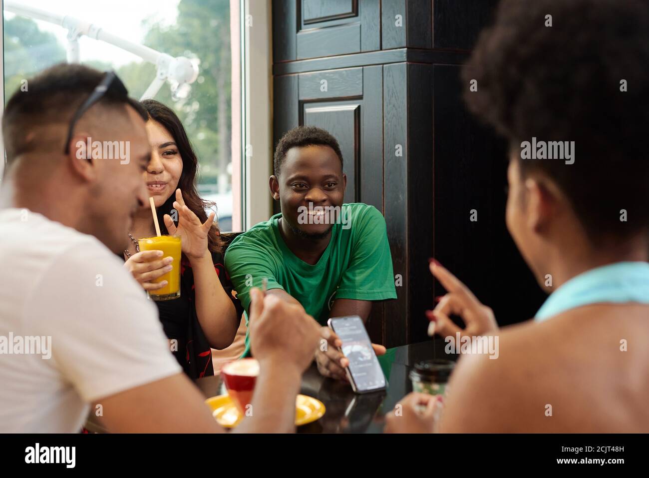 Young black man showing something on the phone screen to his friends while sitting in a cafe. Stock Photo