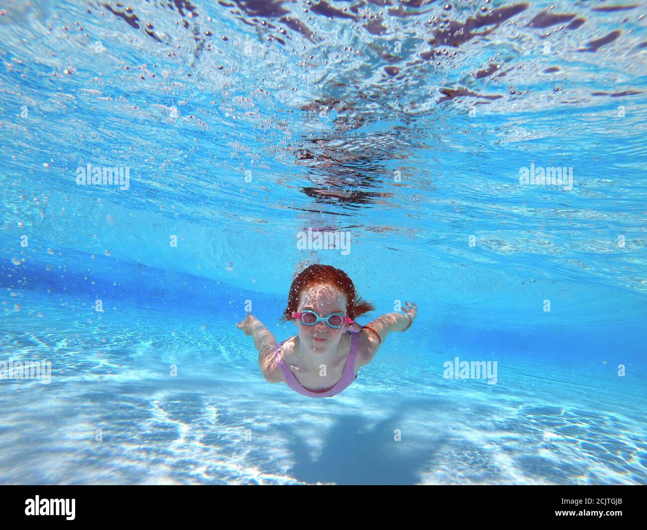 Young Red Headed Girl Swimming Underwater with Goggles in a Pool Stock Photo