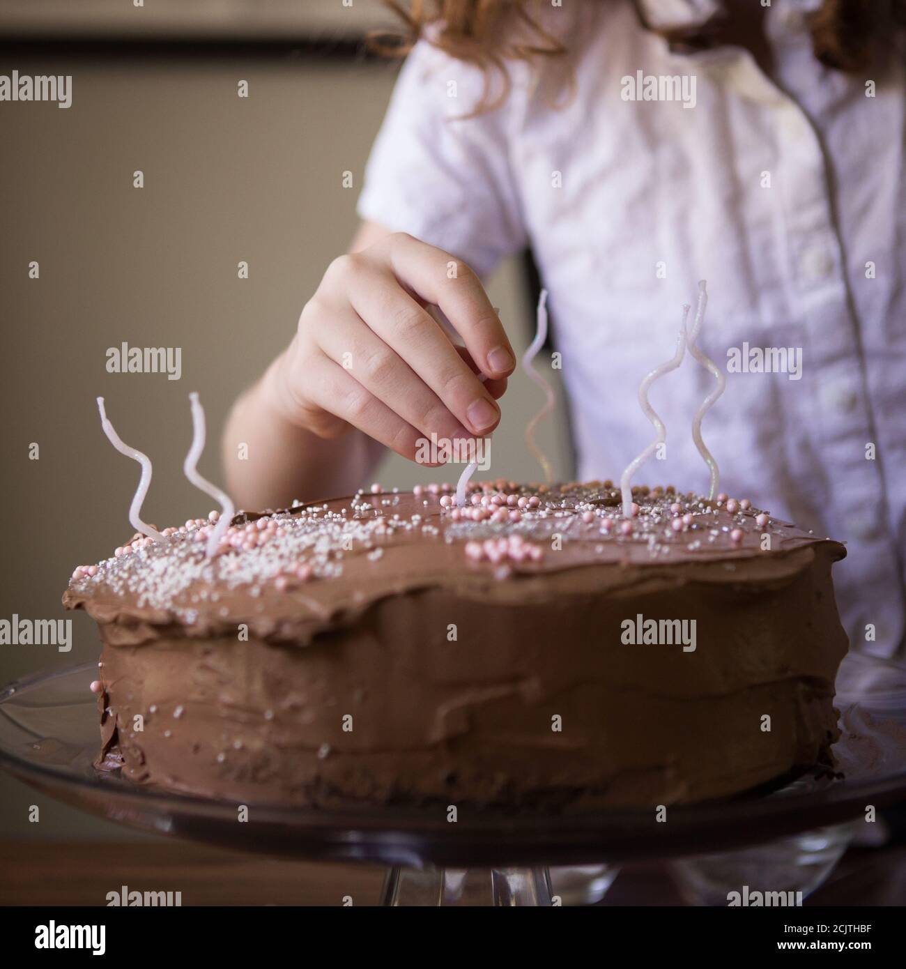 A Young Child Decorating a Chocolate Frosted Birthday Cake with White Candles Stock Photo