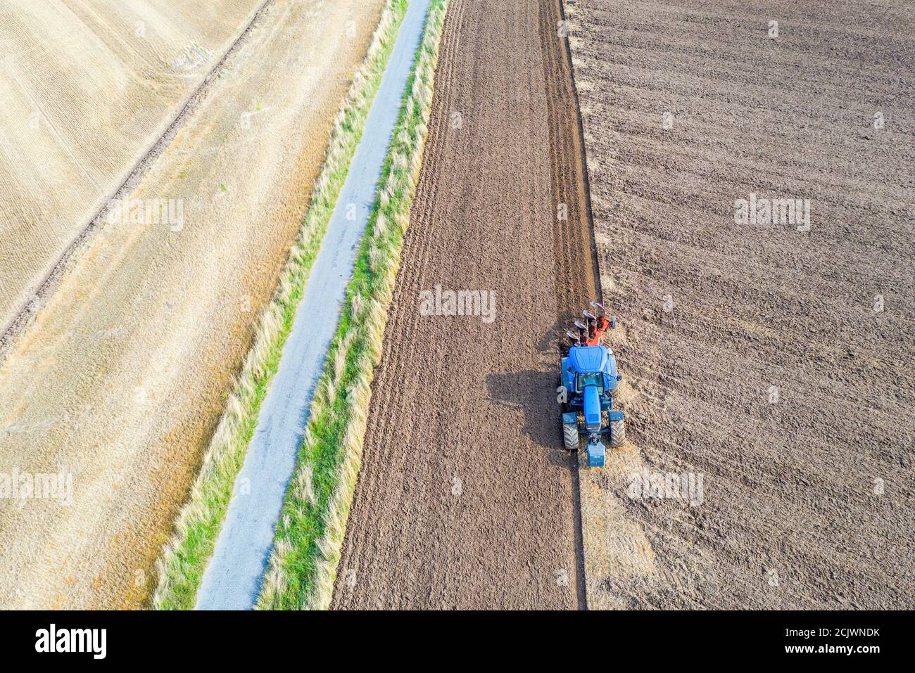 An aerial view of a tractor plowing a barren field for future crops. Stock Photo