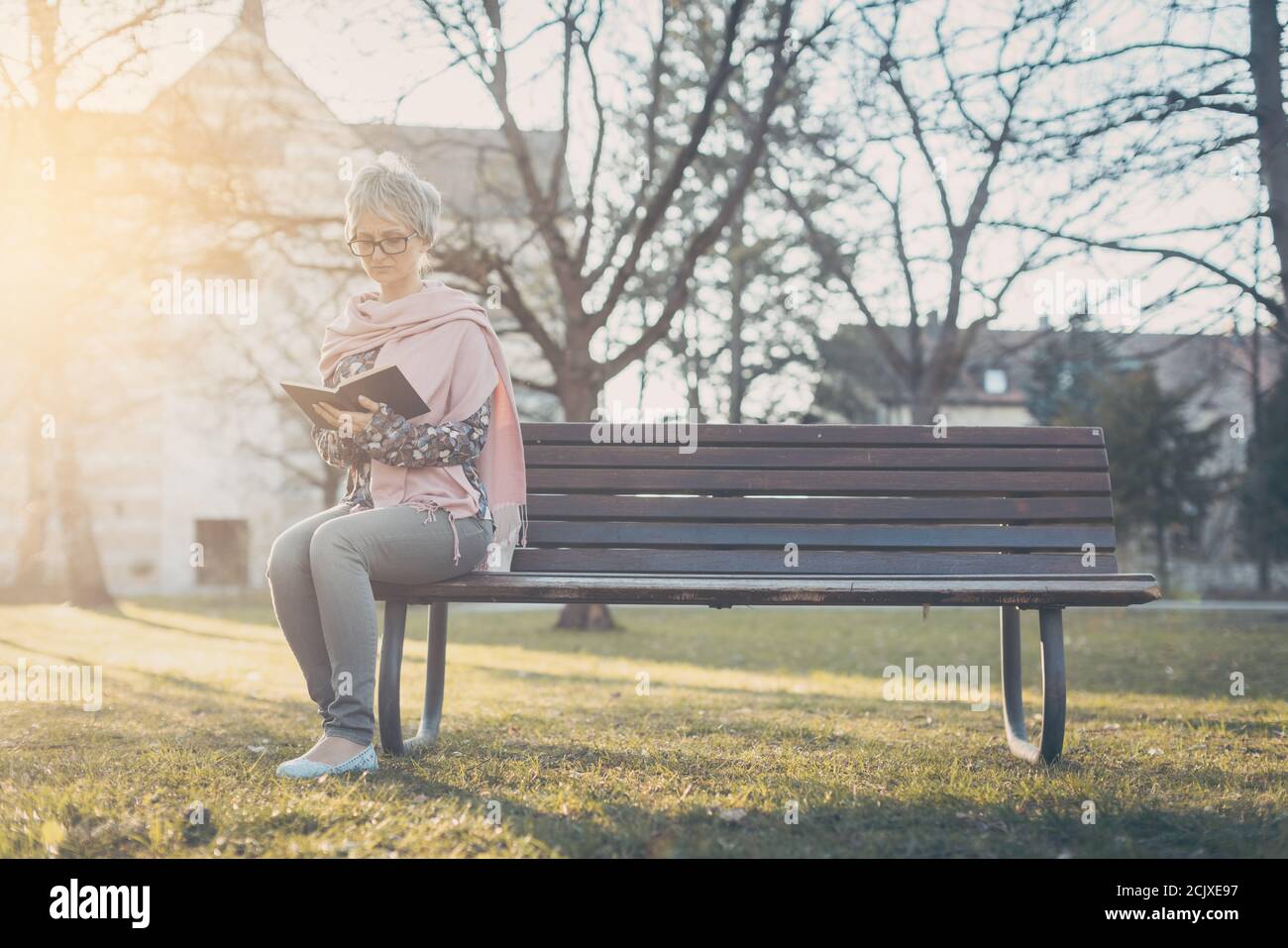 Senior woman sitting alone on bench in the park reading a book Stock ...