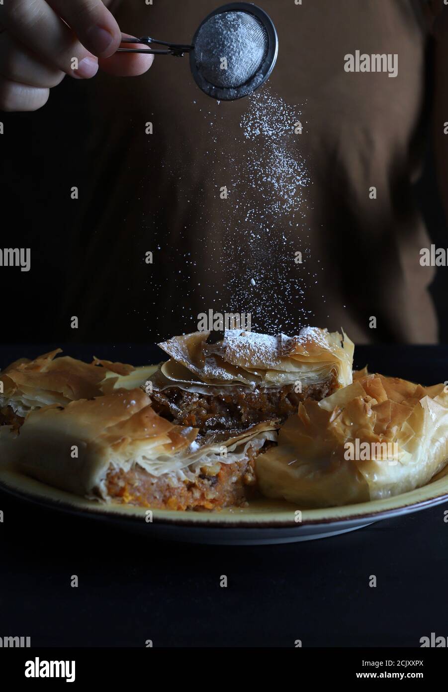 Sprinkled icing sugar on sweet pumpkin pie in phyllo dough. Halloween and fall festivities. Stock Photo