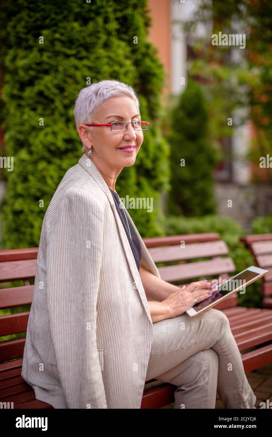 a cheerful grandma is learing to use the tanblet outdoors. side view photo. blurred background Stock Photo