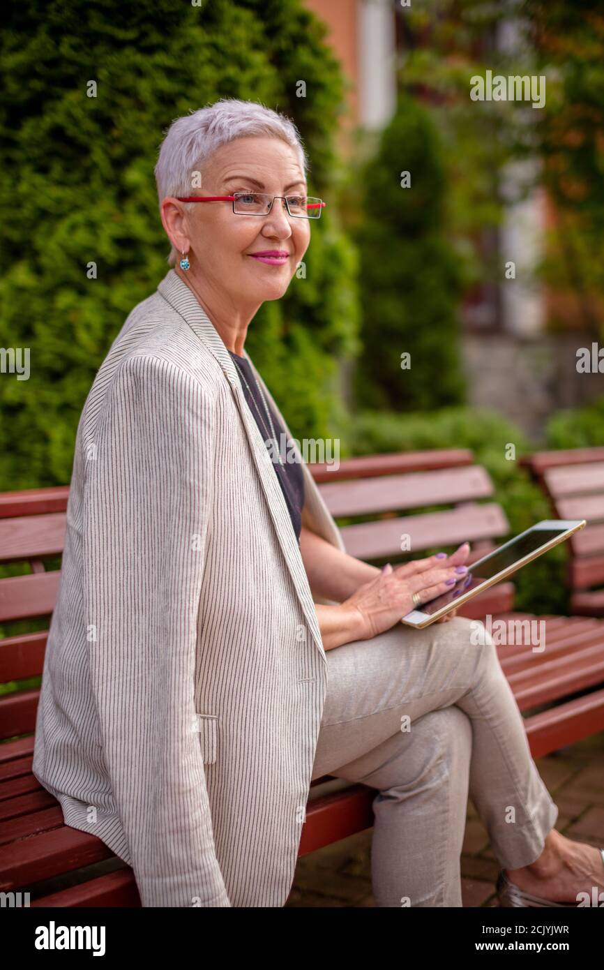 a smiling woman is checking a new tablet while resting in the park. close up side view photo Stock Photo