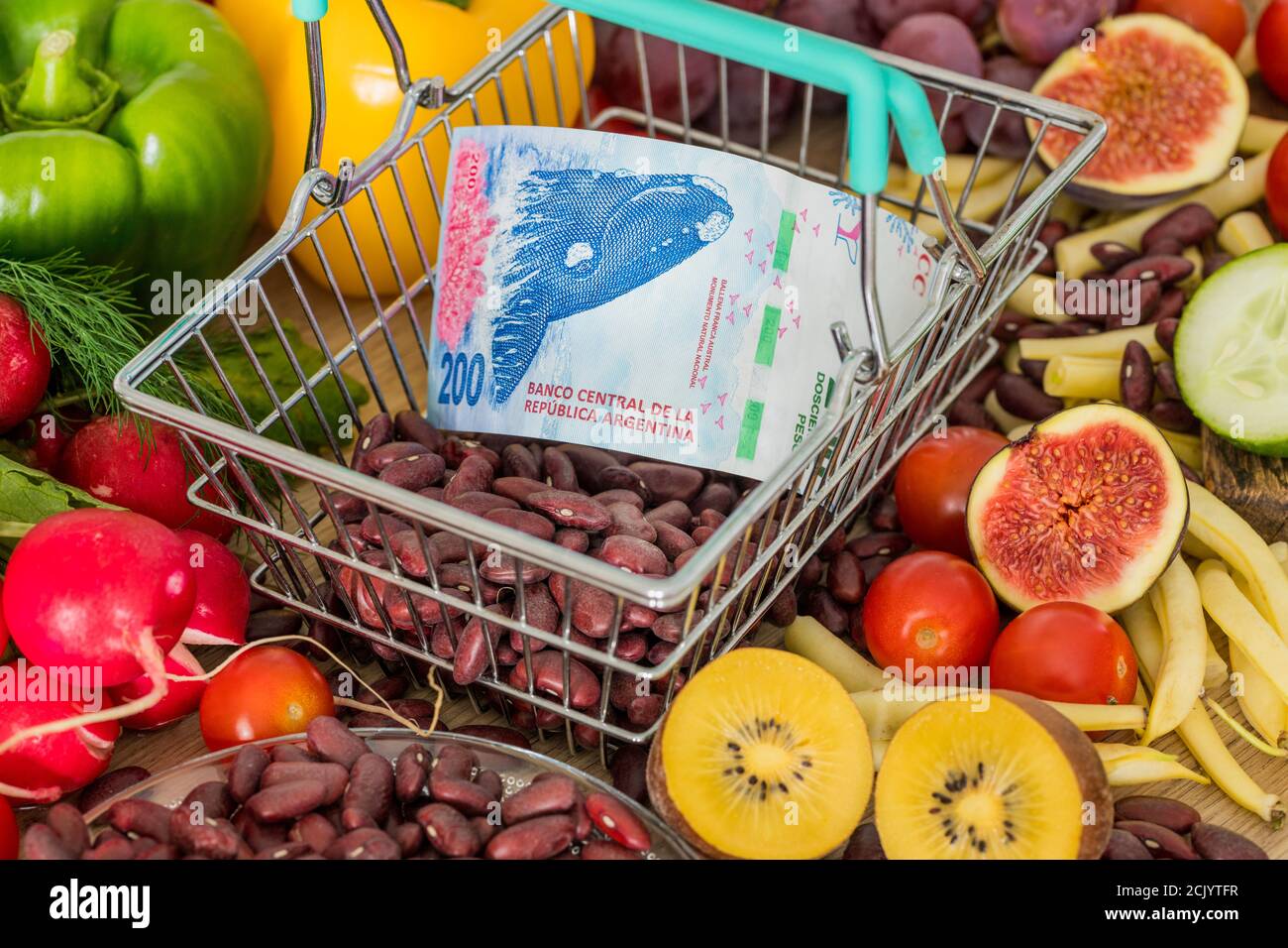 Shopping basket with Argentinian money, around food products, vegetables and fruits. The concept