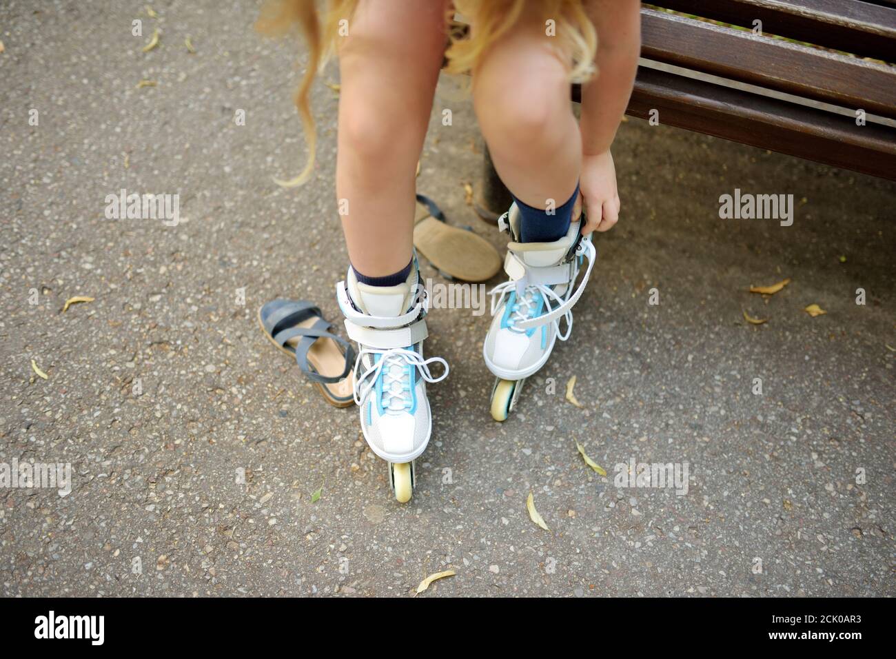 Young girl putting on her inline roller skates on beautiful summer day in a park. Child enjoying