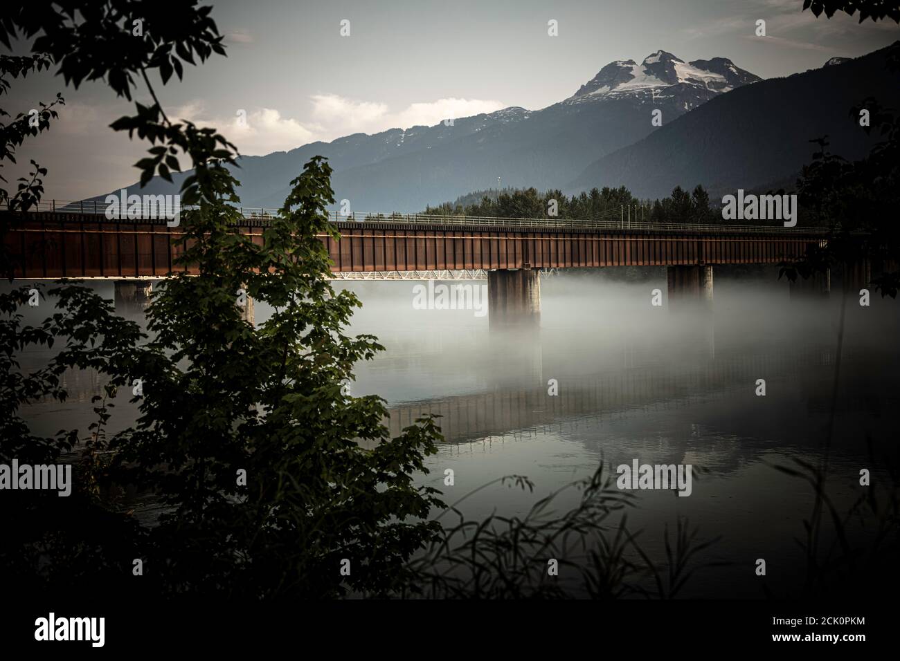 The Revelstoke CP Rail Line bridge over a foggy Columbia river with Begbie Mountain in the Background. Stock Photo