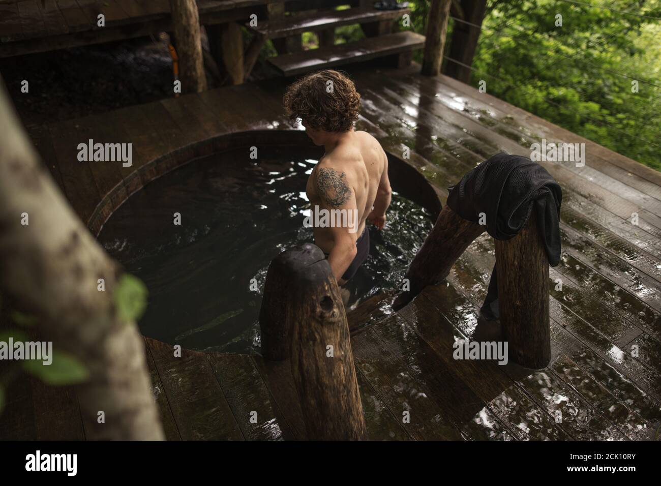 close up top back view photo. healthy guy is standing in the cold waooden bathtub. health improvement concept Stock Photo