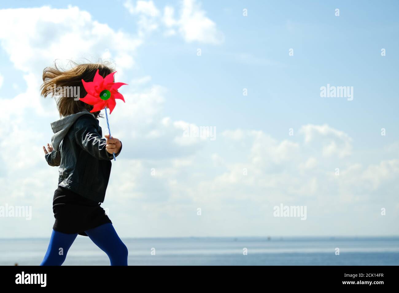 Happy girl with red wind spinner walking on the embankment on blue sky urban background. Freedom concept Stock Photo