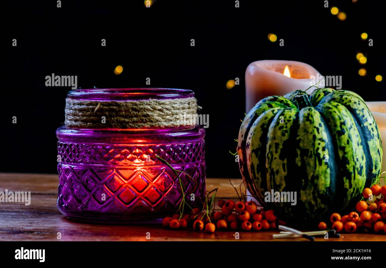 Purple lantern, green pumpkin rowan berries and candle on wooden rustic table and black background with yellow bokeh dots, autumnal warm mood in cozy Stock Photo