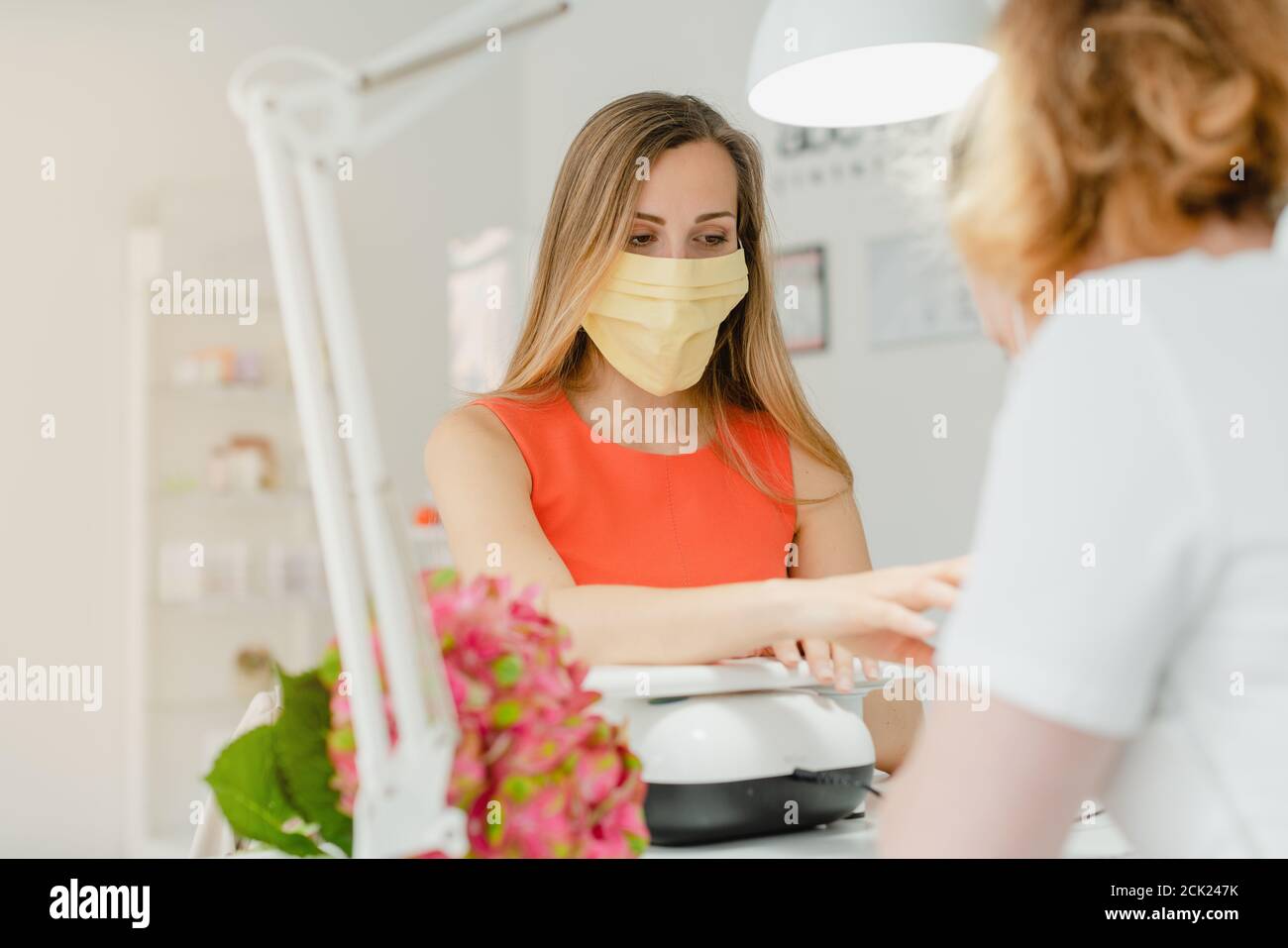 Woman in the nail salon receiving manicure wearing a face mask Stock