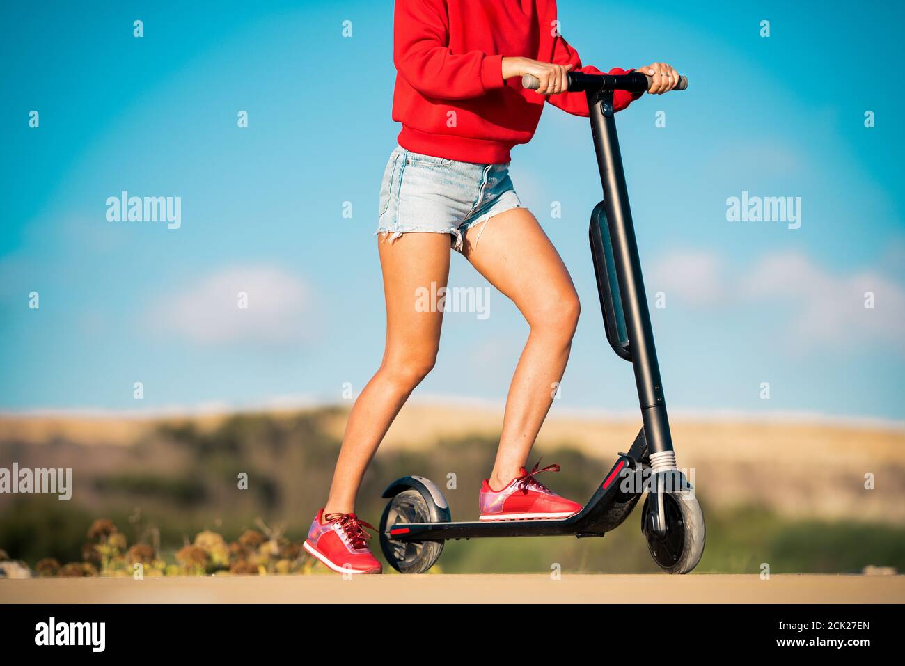 Fit teenage girl in red hoodie and blue denim shorts holding handlebar ...