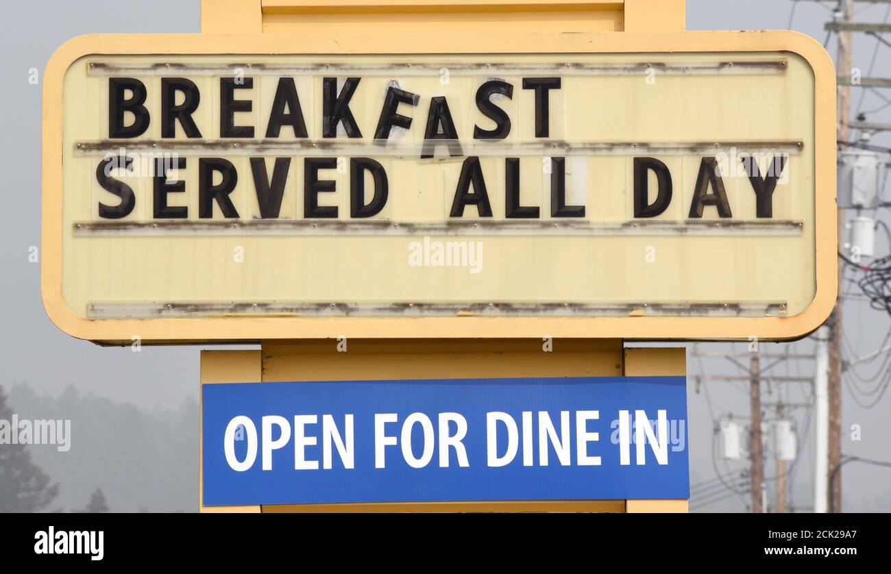 A sign, with letters slipping, says Breakfast Served All Day, and another that says Open For Dine In outside a family style diner restaurant Stock Photo