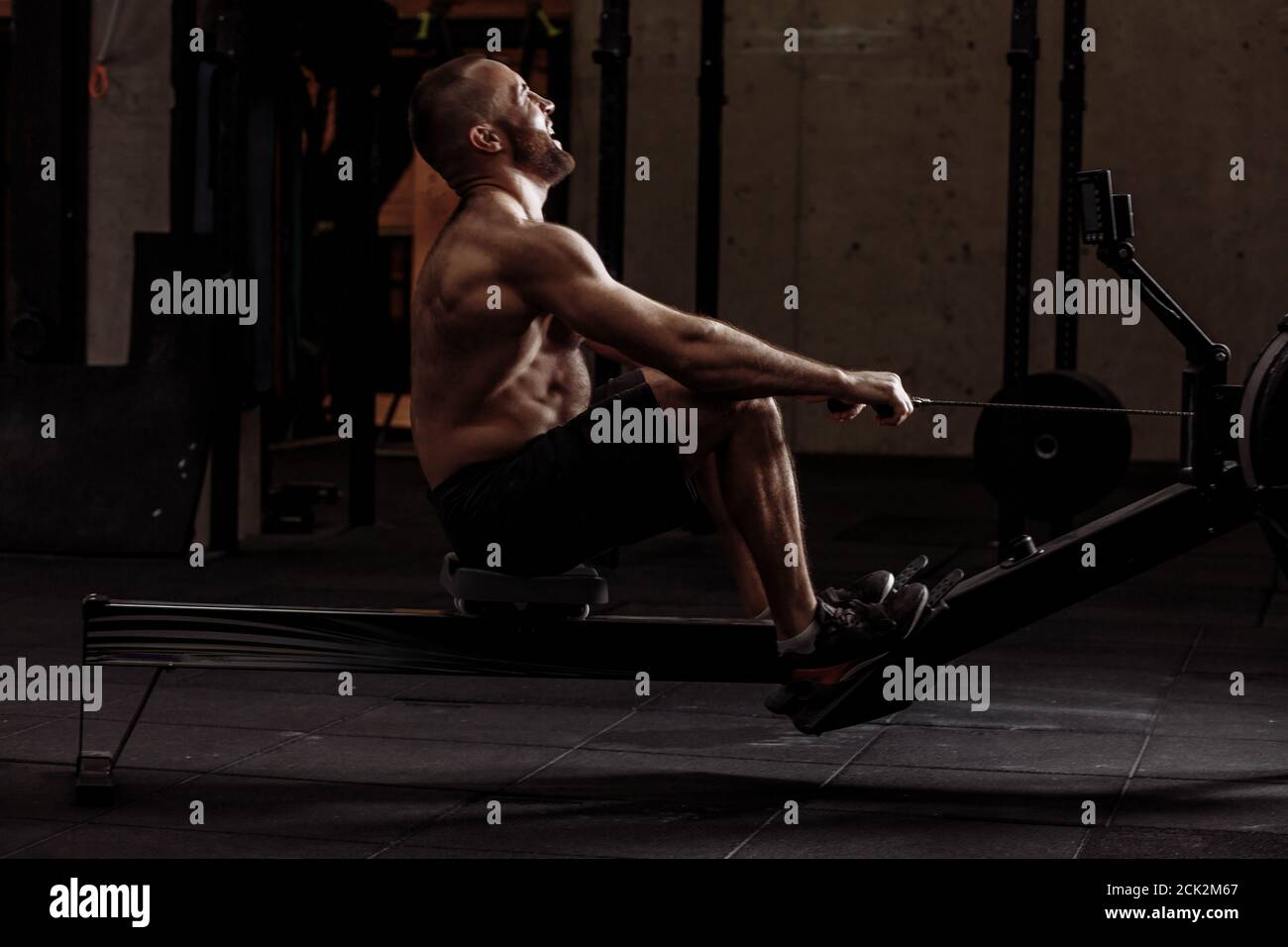 laughing guy is developing his muscles with indoor rower.free time and hobby concept Stock Photo