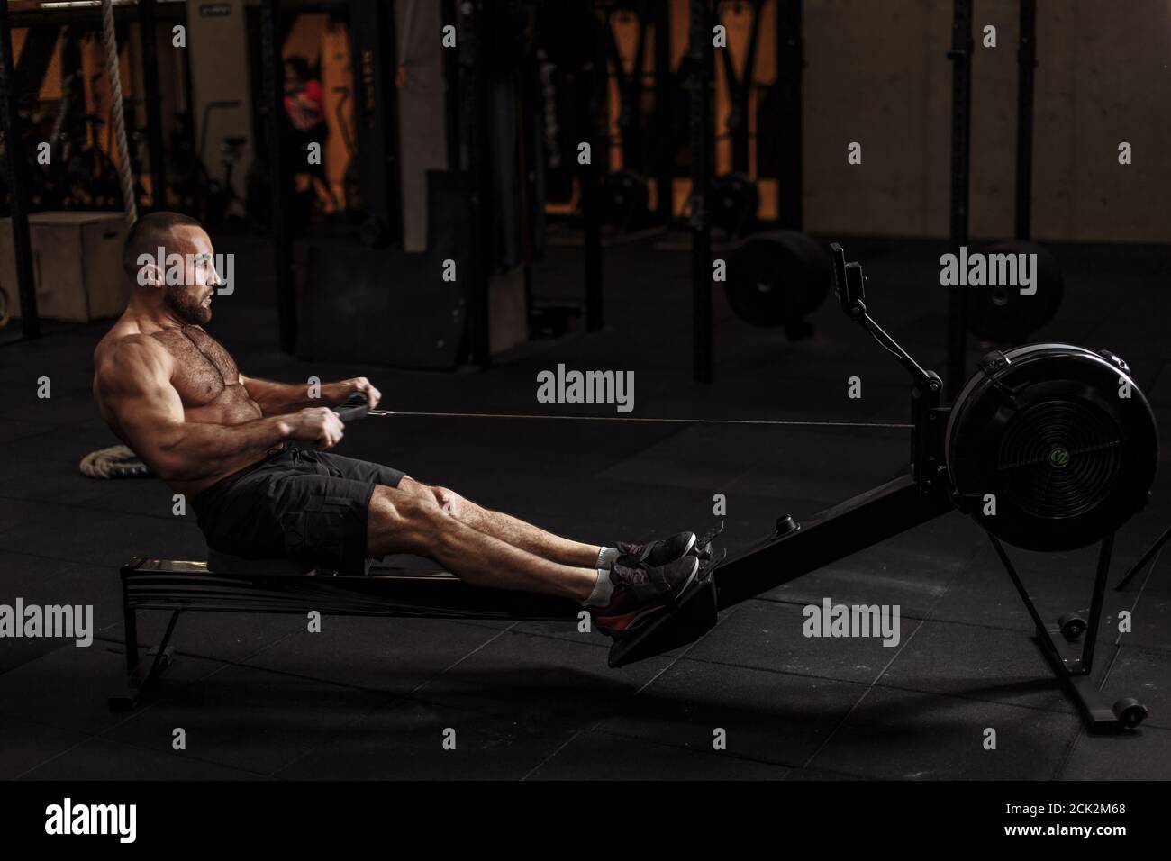 full length side view photo.young fit guy is concentrated on the exercise with indoor rower at gym Stock Photo