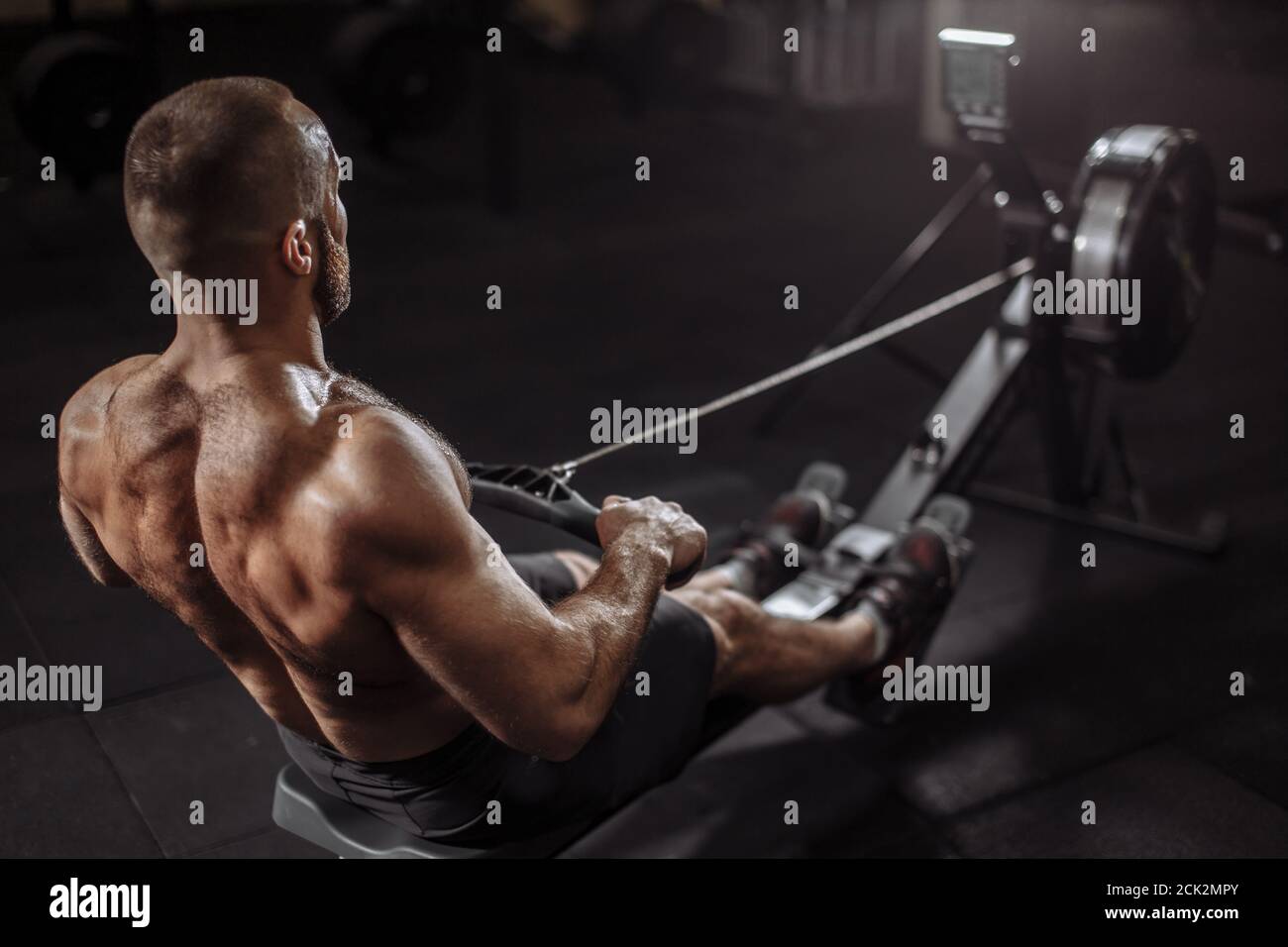 close up back view image. well-built guy is warming up with rowing machine. full length photo Stock Photo