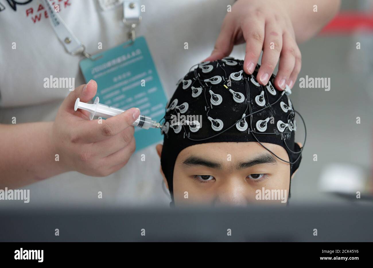 A staff member puts contact gel on the cap of a competitor during a Brain-Computer  Interface (BCI) controlled robot contest at the World Robot Conference  (WRC) in Beijing, China August 17, 2018.