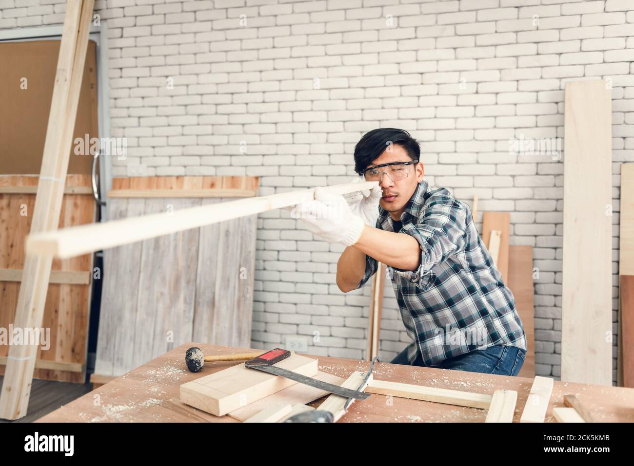 Carpenter Man is Working Timber Woodworking in Carpentry Workshops, Craftsman is Aiming Alignment to Timber Plank for Wooden Furniture in Workshop. DI Stock Photo