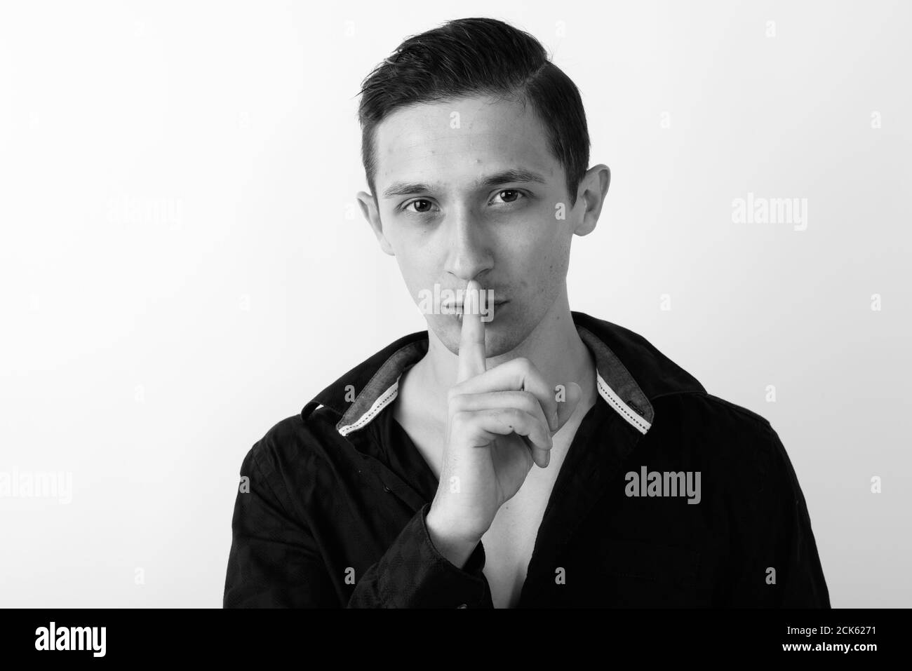 Close up of young handsome man with finger on lips and shirt open against white background Stock Photo