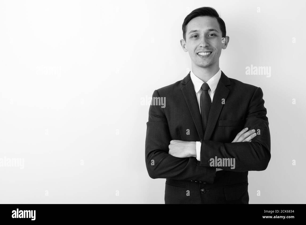 Studio shot of young happy businessman smiling with arms crossed ...
