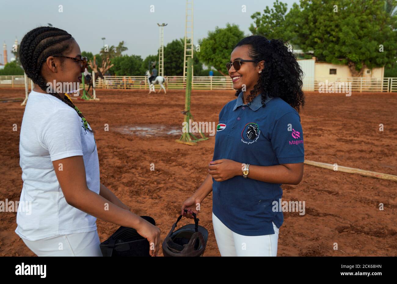 Rayan (L), 24, and her friend Sagda, 24, chat before horse riding at the Equestrian Club, in Khartoum, Sudan, July 2, 2019. Rayan has been riding for 13 years. She was a gymnast and had a show at the club, where she saw horses and decided she wanted to ride. She is also a football player. Sagda, a journalist and club member who had been riding for 11 years, said: 'My mum brought me here, my family don't mind that I'm a woman riding. 'It can be a bit hard - some people disapprove at how we are dressed,' she added, alluding to tight-fitting equestrian garb. REUTERS/Andreea Campeanu  SEARCH 'CAMP Stock Photo