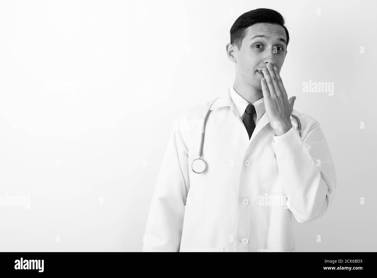 Studio shot of young handsome man doctor covering mouth with hand against white background Stock Photo
