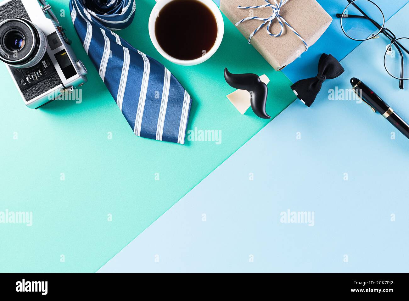 Happy Fathers Day background concept with coffee cup, decorated bowtie, necktie, eyeglasses, gift box and mustache on bright pastel background. Stock Photo
