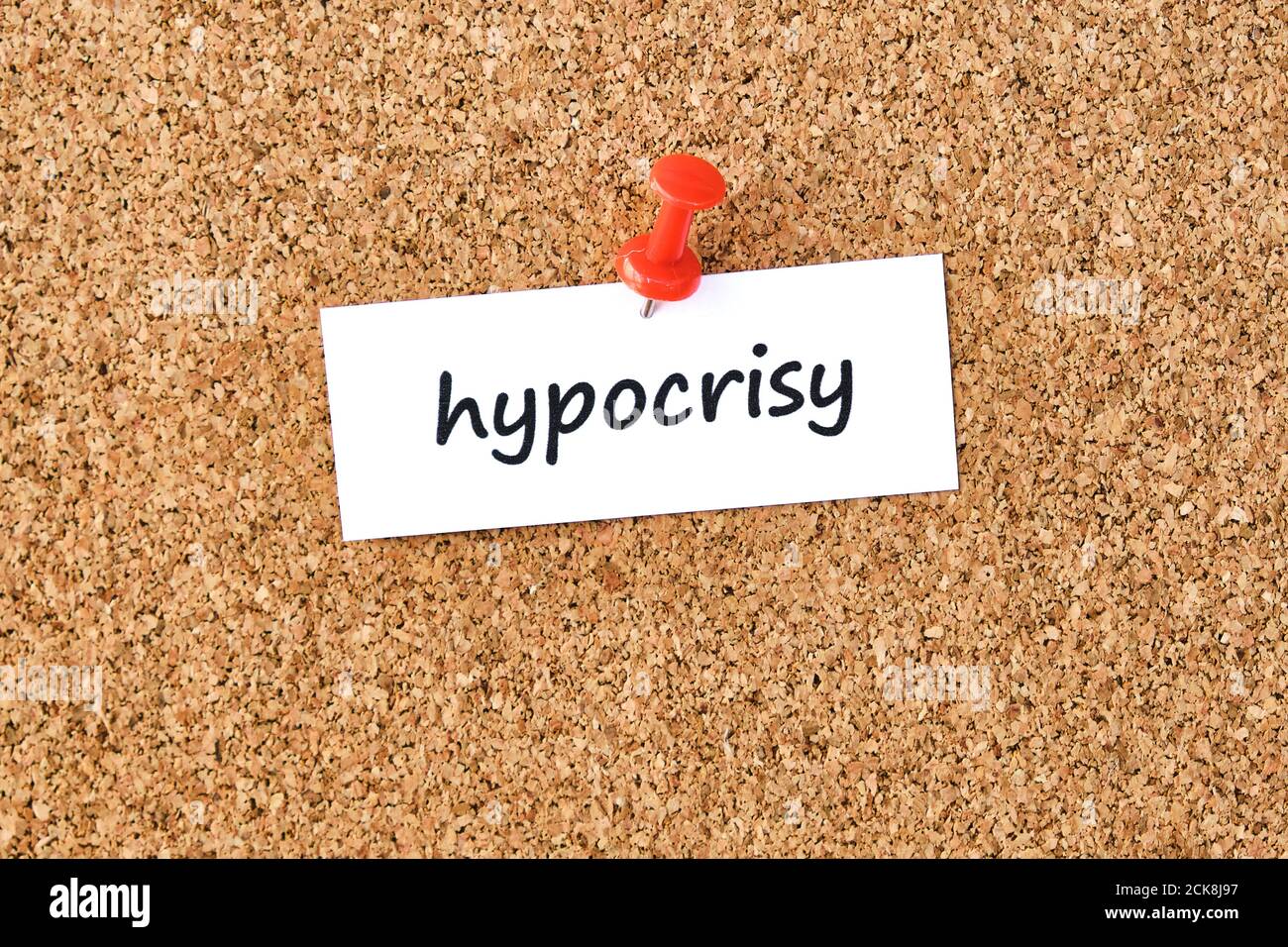 Hypocrisy. Word written on a piece of paper or note, cork board background. Stock Photo
