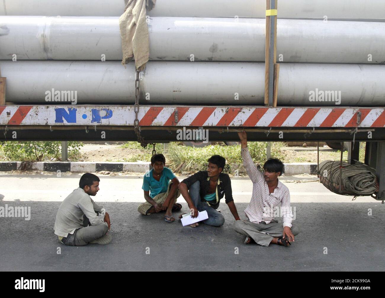 Truck drivers and helpers sit under a parked truck while waiting to get their loads cleared to cross a checkpoint at the Commercial Taxes Department check post at Walayar in Palakkad district in southern Indian state of Kerala, India, September 5, 2015. At the Walayar checkpoint in southern India, lines of idle trucks stretch as far as the eye can see in both directions along the tree-lined interstate highway, waiting for clearance from tax inspectors that can take days to complete. The rollout of a nationwide goods and services tax (GST) from April was supposed to sweep away hundreds of check Stock Photo