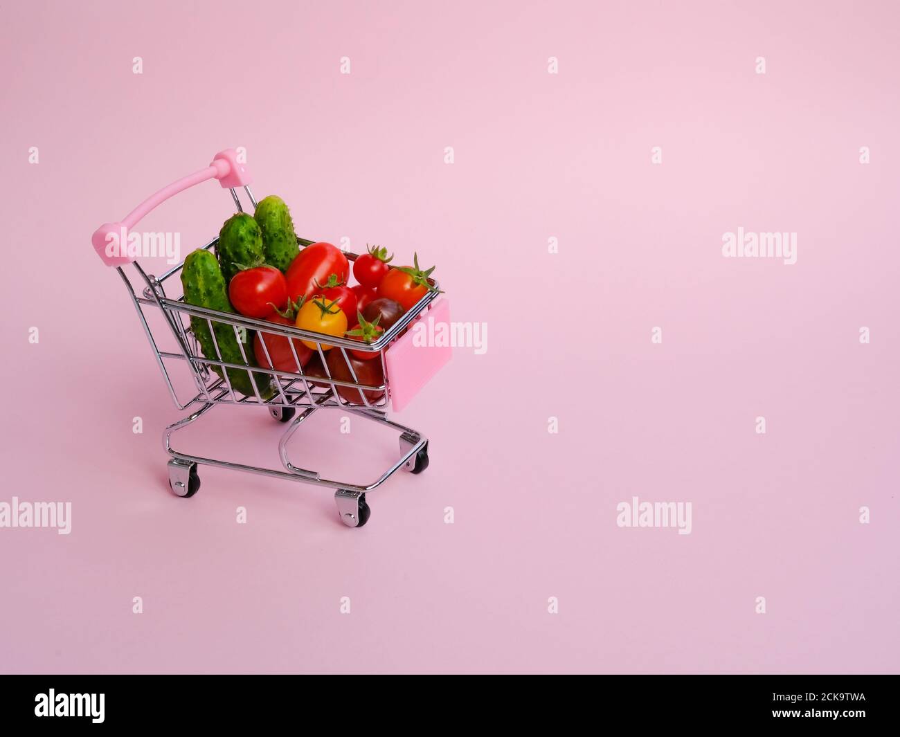 Pink grocery cart full of tomatoes and cucumbers on pink background Stock Photo