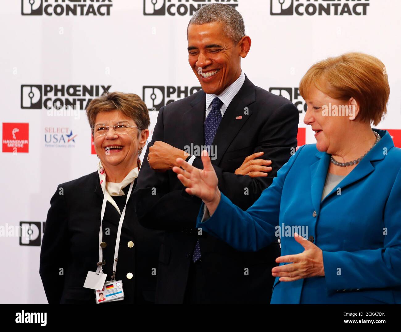 U S President Barack Obama C German Chancellor Angela Merkel And Interpreter Brigitta Richman L React At The Booth Of Phoenix Contact During The Opening Tour Of The Hannover Messe In Hanover Germany