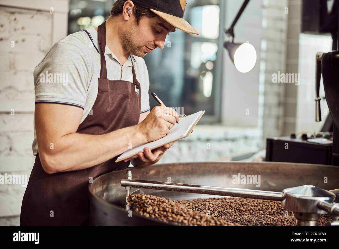 Handsome man taking notes while using coffee roasting machine Stock Photo