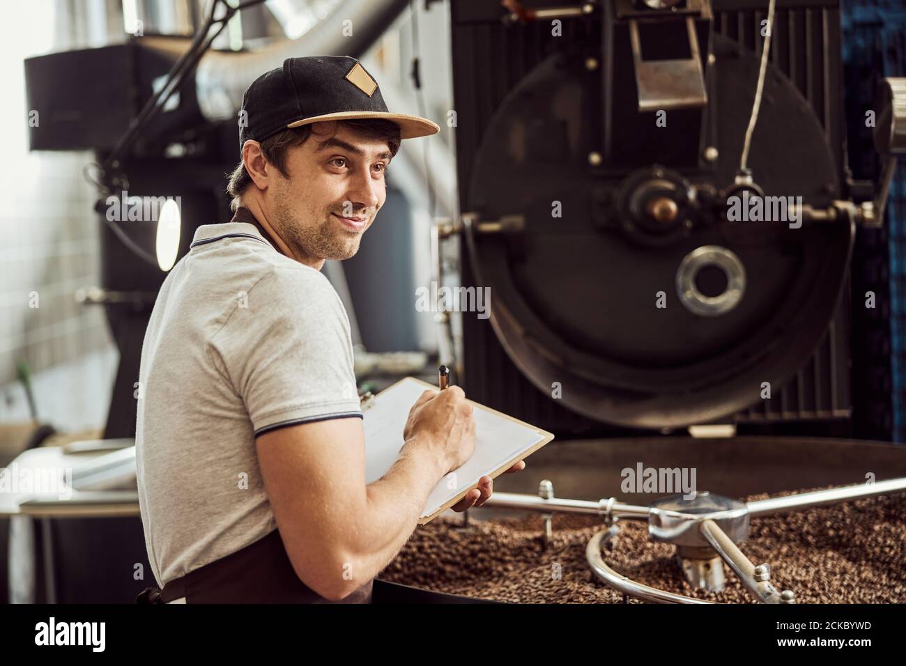 Joyful male worker taking notes while using coffee roasting machine Stock Photo