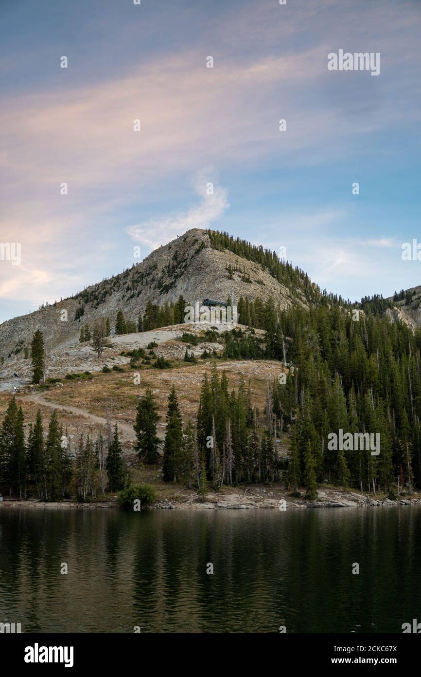 Vertical shot of a lake surrounded by hills and greenery under a blue ...