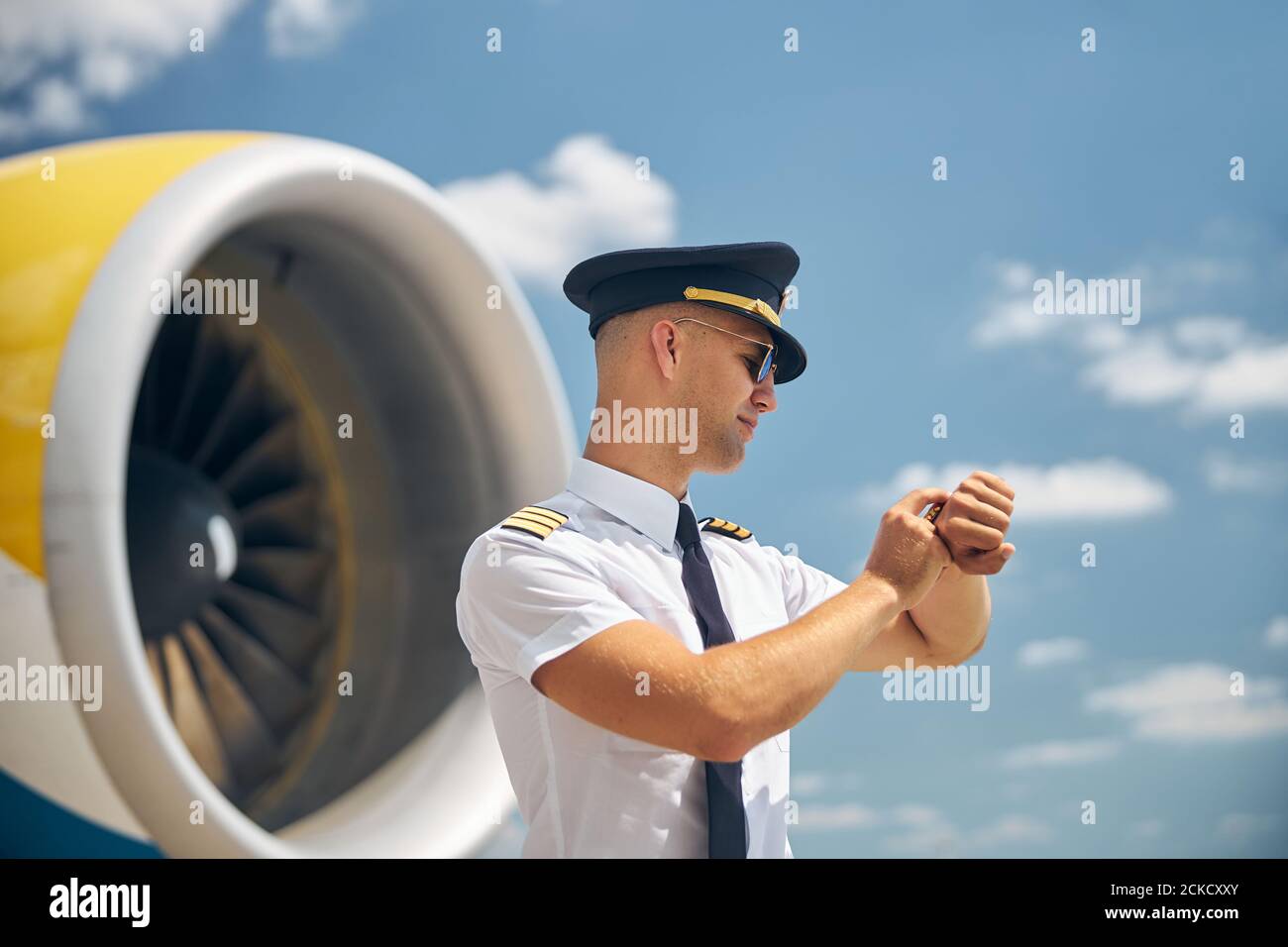 Handsome male pilot looking at wristwatch at airfield Stock Photo