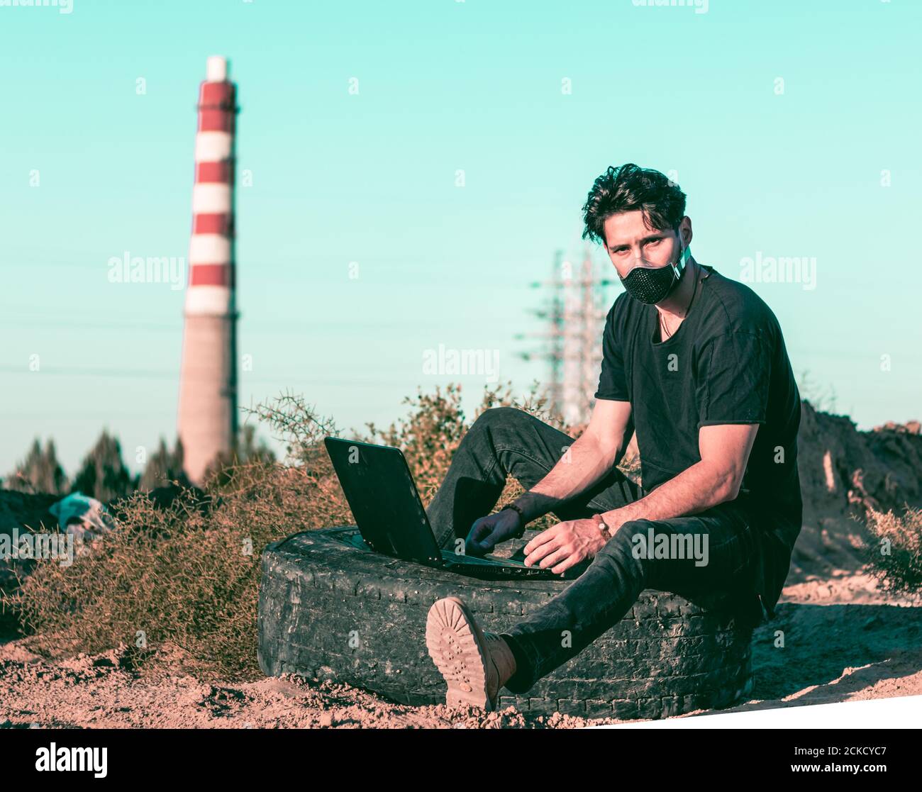 A physically distant and socially connected young man in a black outfit in an industrial zone Stock Photo
