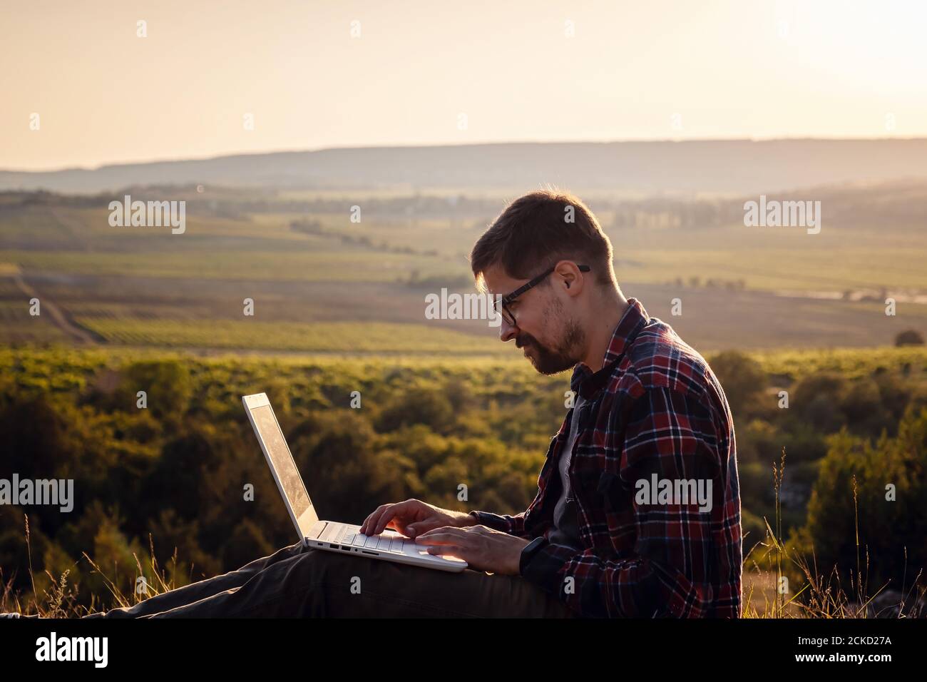 man with laptop sitting on the edge of a mountain with stunning views of the valley. Cellular network broaband coverage concept. 5G. Stock Photo