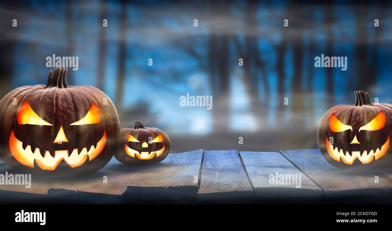 Three Spooky Halloween Pumpkins Jack O Lantern With Evil Face And Eyes On A Wooden Bench Table With A Misty Night Forest Background With Space For Stock Photo Alamy