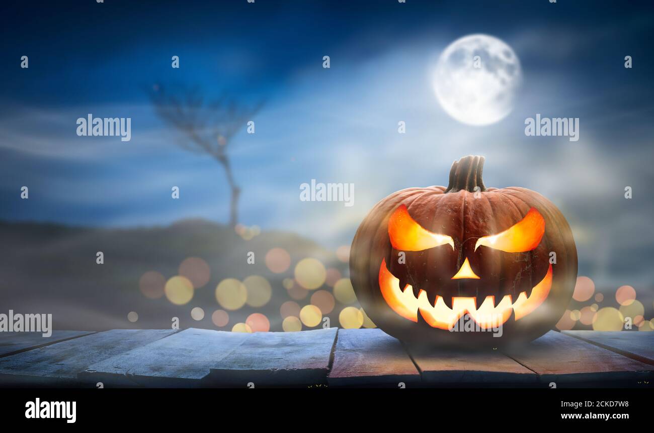 One spooky halloween pumpkin, Jack O Lantern, with an evil face and eyes on a wooden bench, table with a misty night background with space for product Stock Photo