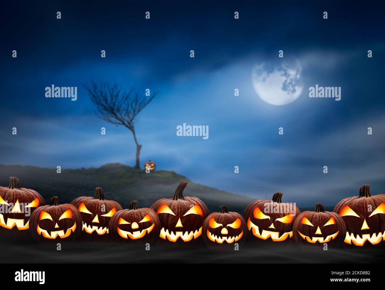 Lots of halloween lanterns with evil face and eyes, Jack O Lantern, against a spooky looking landscape background at night with a glowing full moon, l Stock Photo