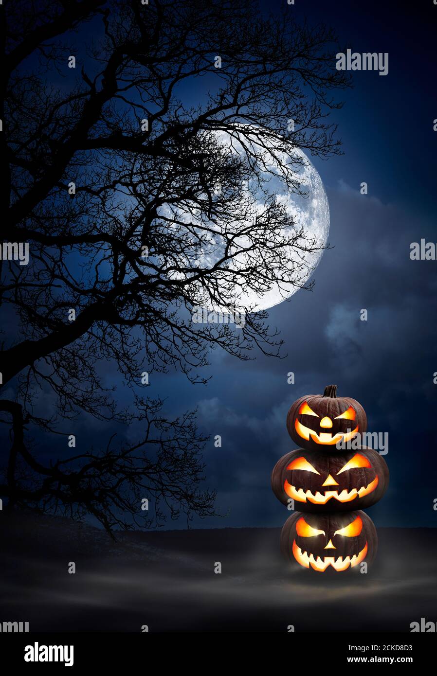 A Pile Of Three Spooky Halloween Pumpkins Jack O Lantern With Evil Face And Eyes Under The Silhouette Of A Tree At Night With A Full Moon And Misty Stock Photo