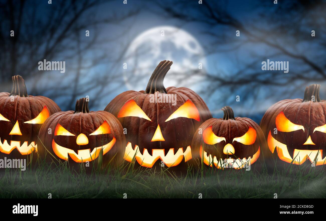 Five spooky halloween pumpkin, Jack O Lantern, with an evil face and eyes on the grass with a misty night sky background with a full moon. Stock Photo