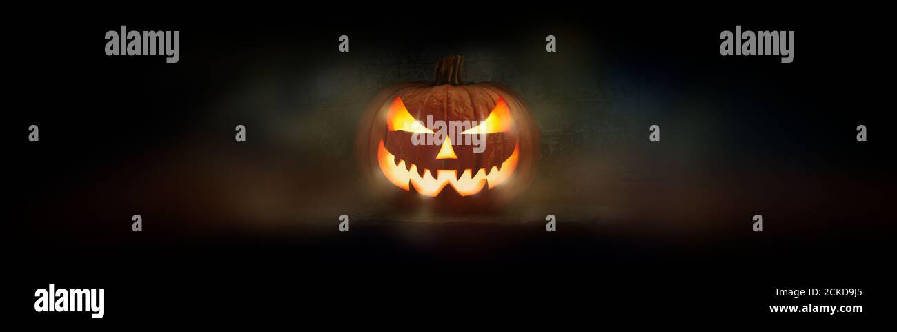 One spooky evil halloween lantern, Jack O Lantern, with glowing eyes and face on a dark background. Stock Photo