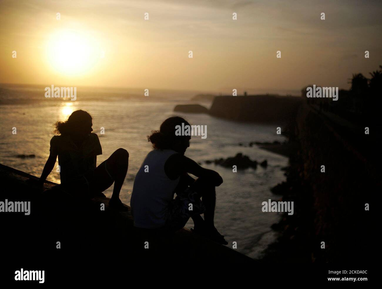People sit on the edge of a lookout on the walls of the 16th century Dutch fort as the sun sets in Galle July 8, 2009. REUTERS/Vivek Prakash (SRI LANKA SOCIETY TRAVEL) Stock Photo